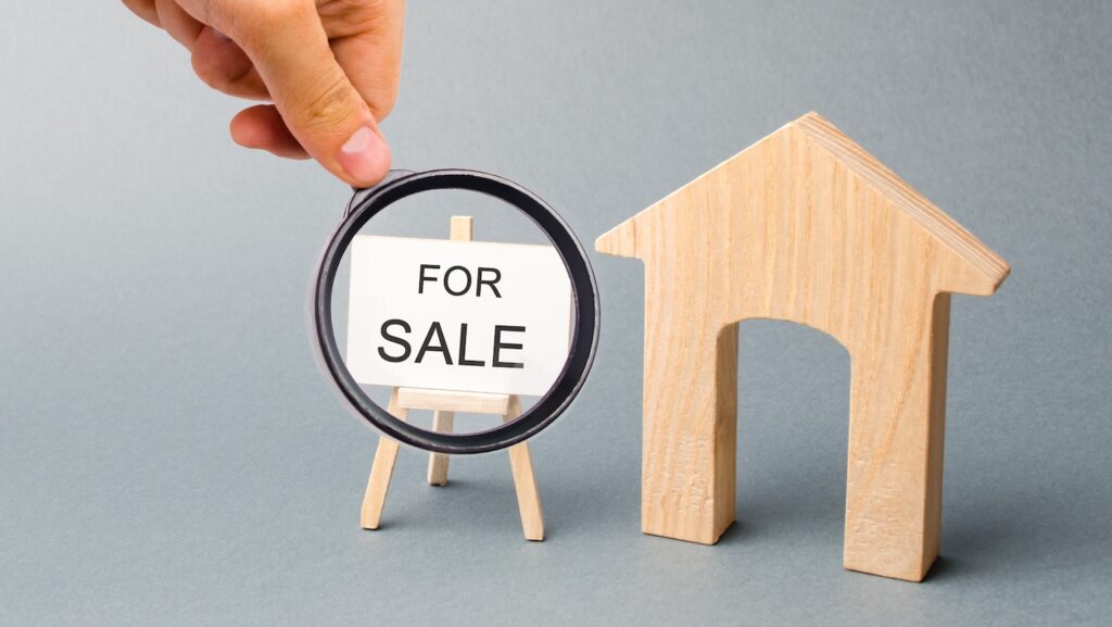 A miniature wooden house and a poster with the word For Sale